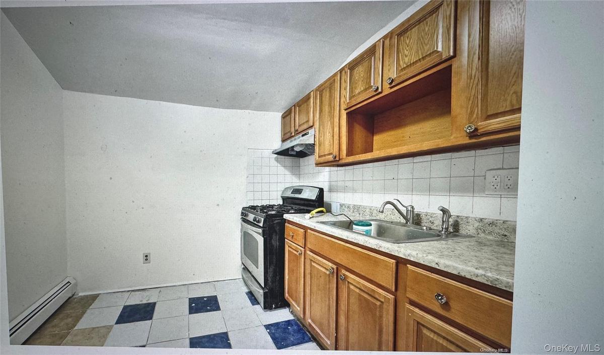 Kitchen featuring backsplash, brown cabinetry, a baseboard heating unit, gas range, and light countertops