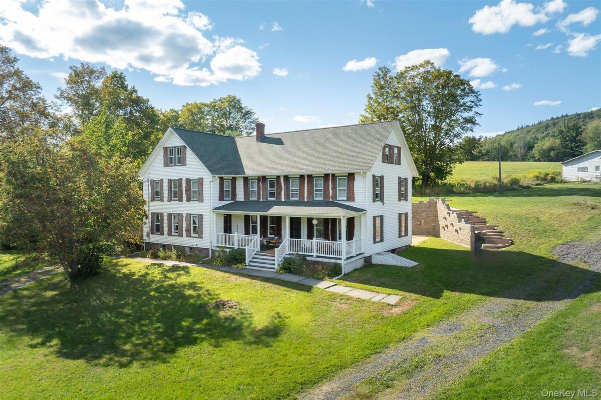 Colonial home featuring covered porch, a chimney, a front lawn, and roof with shingles