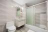 Full bathroom with tile walls, shower / bath combination with glass door, toilet, and vanity