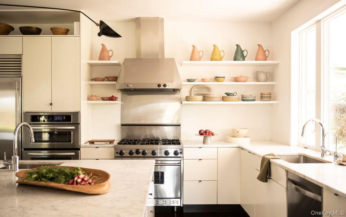 Kitchen with open shelves, wall chimney range hood, high end appliances, light stone counters, and modern cabinets