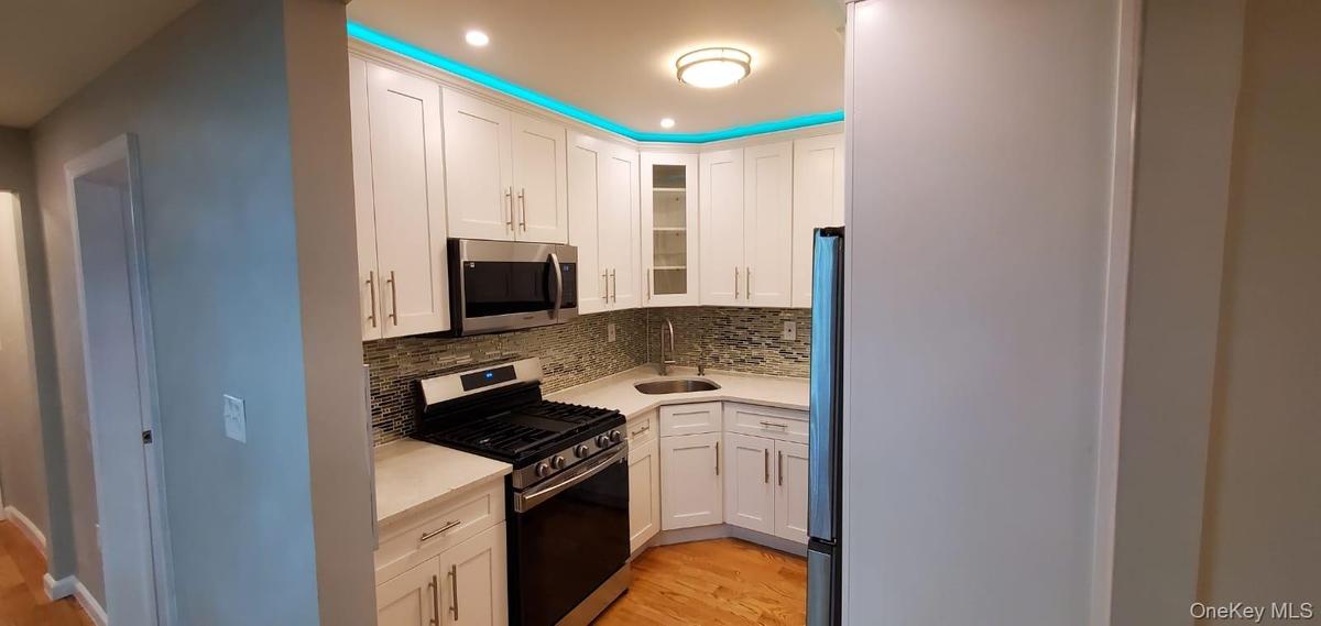 Kitchen with appliances with stainless steel finishes, white cabinets, light stone counters, glass insert cabinets, and light wood finished floors