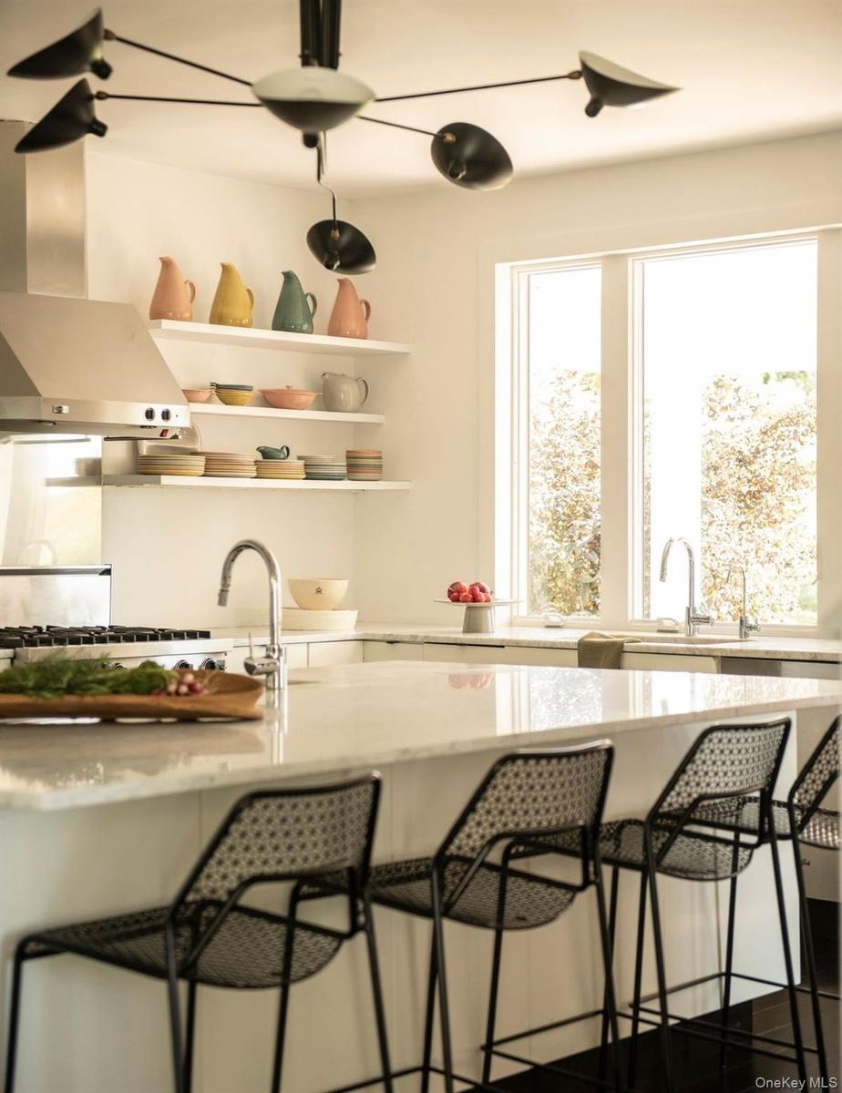Bar area with light stone counters, wall chimney range hood, open shelves, and white cabinetry