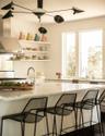 Bar area with light stone counters, wall chimney range hood, open shelves, and white cabinetry