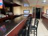Community bar area featuring light tile patterned floors, dark stone countertops, a wainscoted wall, and a drop ceiling