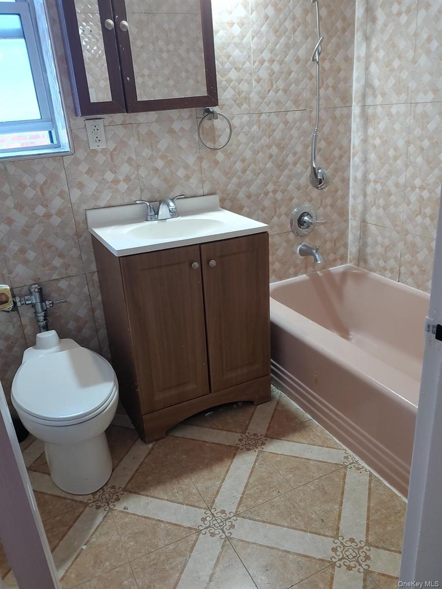 Full bathroom with tile walls, shower / bathtub combination, vanity, inlaid floor details, and tasteful backsplash