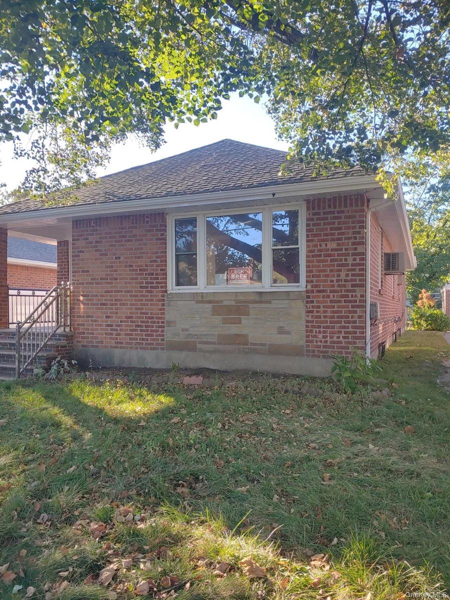 View of side of home featuring a lawn, brick siding, and a shingled roof