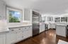 Kitchen with white cabinets, appliances with stainless steel finishes, light stone countertops, dark wood-style floors, and decorative backsplash