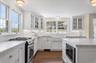 Kitchen featuring stainless steel gas range, glass insert cabinets, white cabinetry, and light stone counters