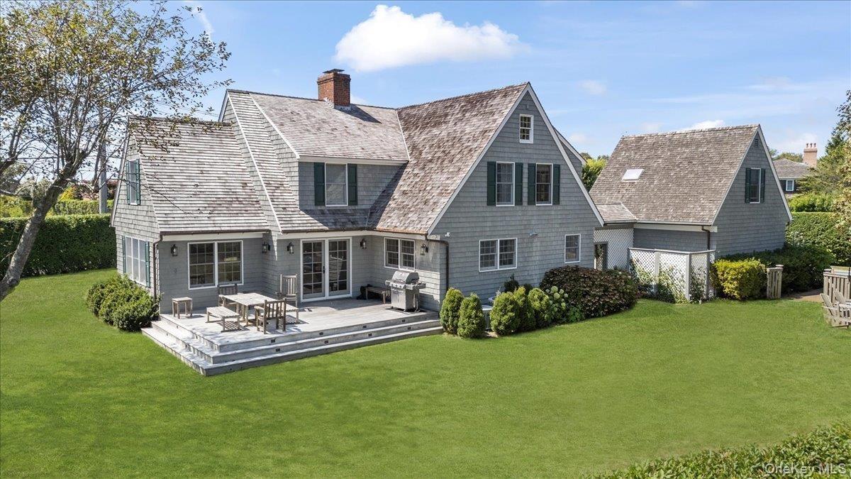 Rear view of house featuring a yard, a chimney, and a wooden deck