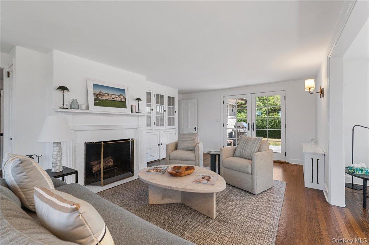 Living room with wood finished floors, a fireplace with flush hearth, and french doors