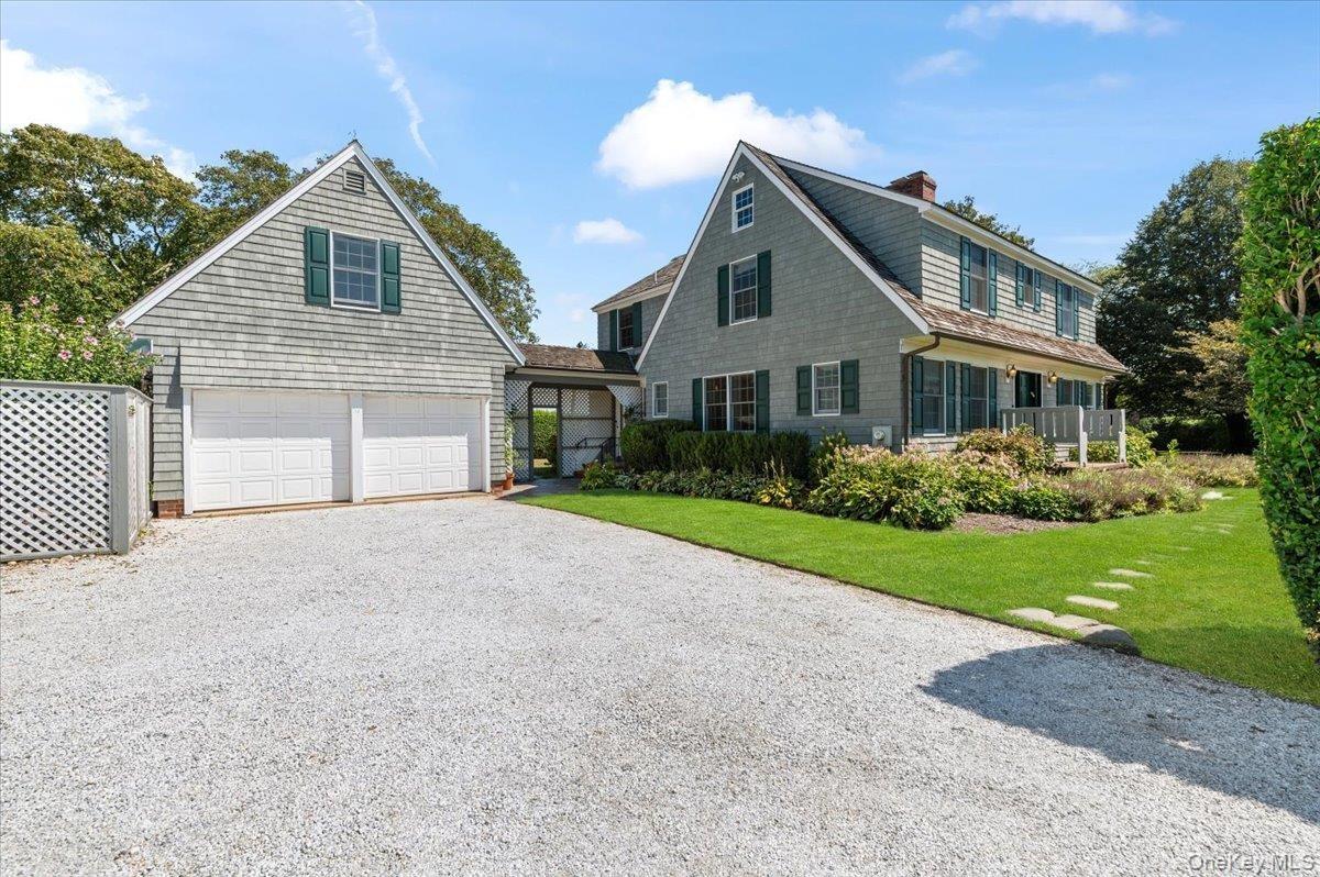 View of front of house featuring driveway, a front lawn, a chimney, and an attached garage