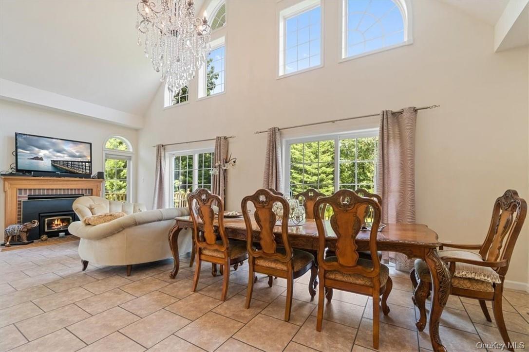 Tiled dining room with an inviting chandelier, a brick fireplace, a healthy amount of sunlight, and a towering ceiling