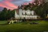 Back house at dusk with a wooden deck and a lawn