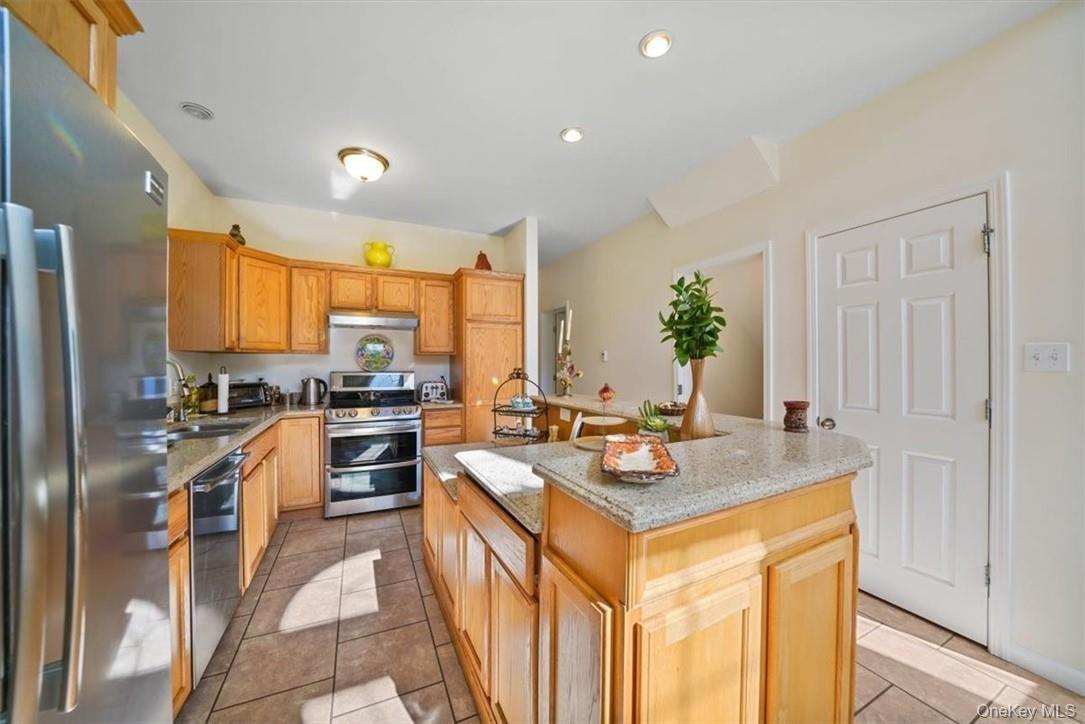 Kitchen with appliances with stainless steel finishes, light tile patterned floors, sink, and a kitchen island