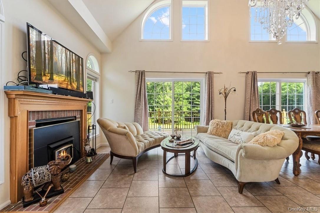 Tiled living room with a brick fireplace, high vaulted ceiling, and an inviting chandelier