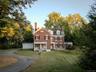 Colonial-style house with a chimney, a front yard, brick siding, driveway, and view of scattered trees