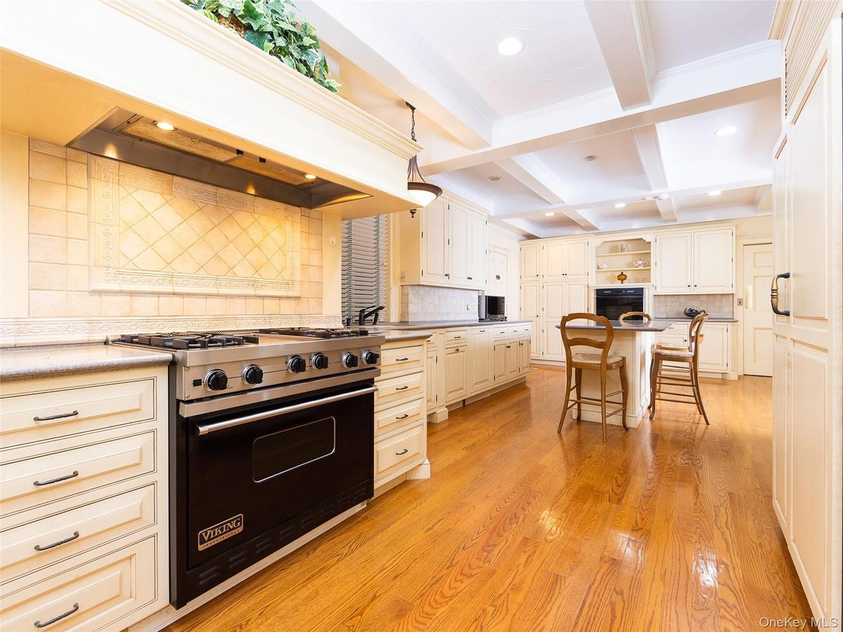 Kitchen featuring tasteful backsplash, a breakfast bar area, open shelves, black appliances, and premium range hood