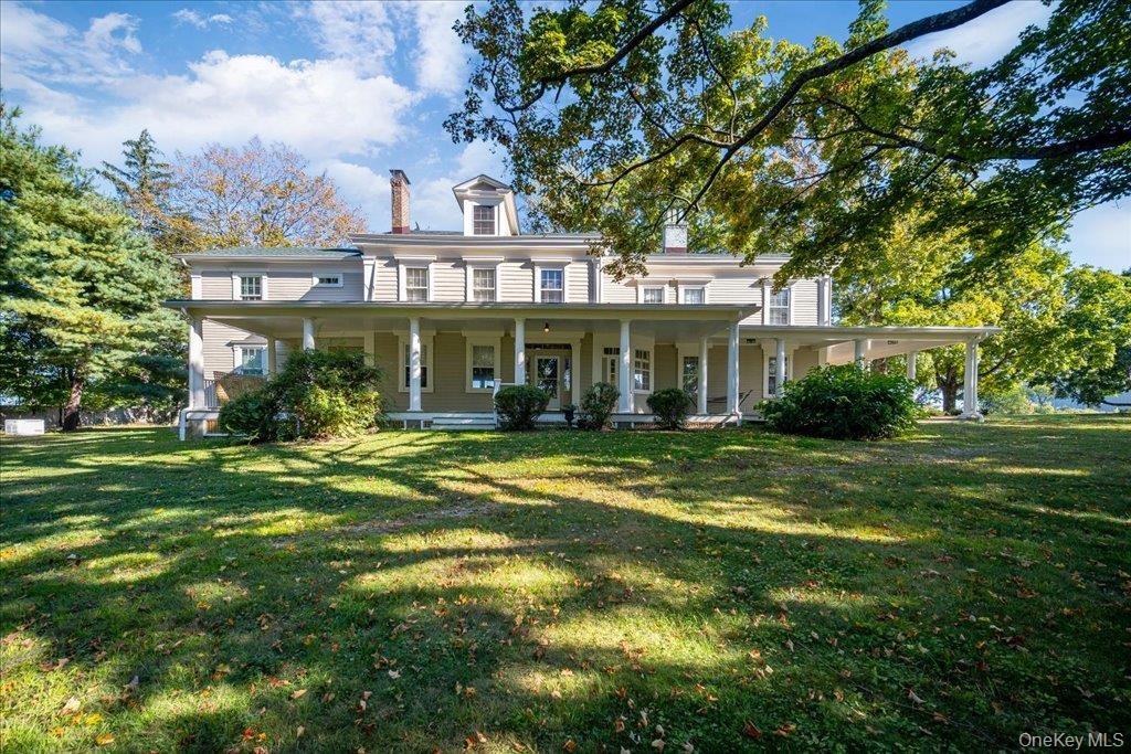 View of front facade featuring a chimney, covered porch, and a front yard