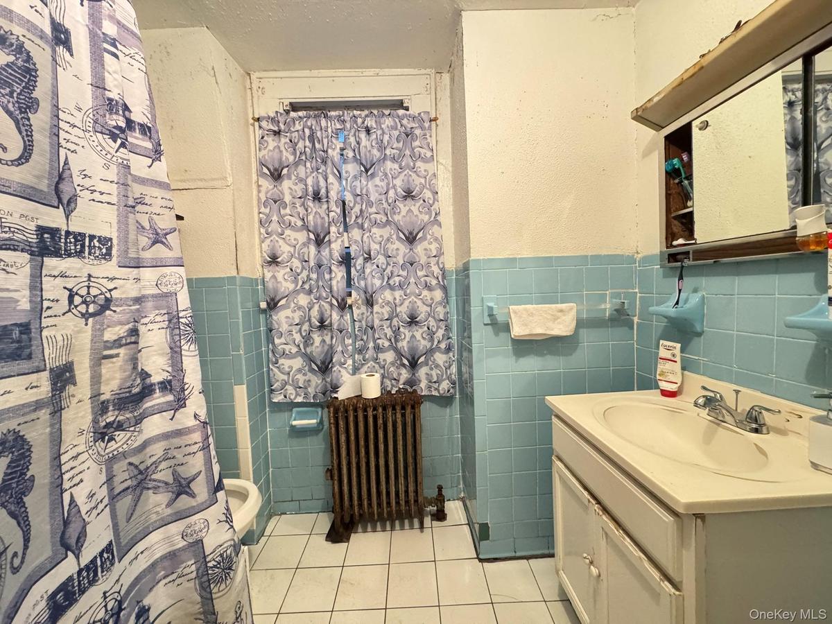 Full bathroom featuring light tile patterned floors, tile walls, vanity, wainscoting, and radiator