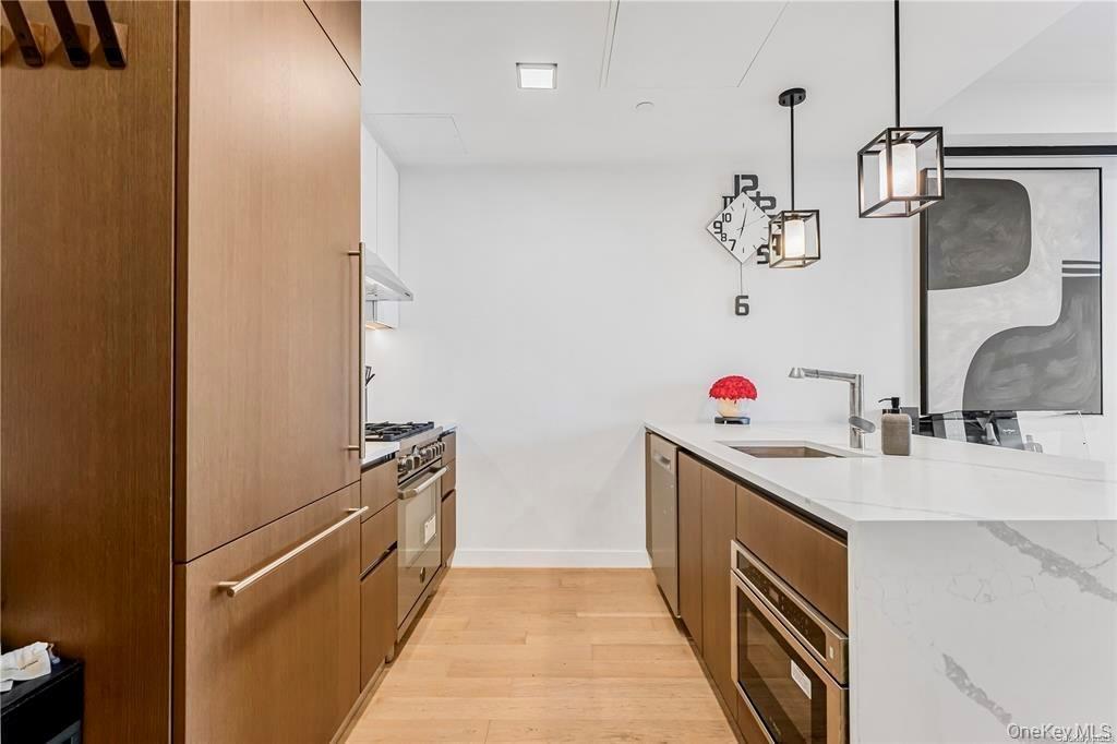 Kitchen featuring a peninsula, light stone countertops, light wood-type flooring, decorative light fixtures, and modern cabinets