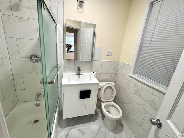 Bathroom with vanity, shower / bath combination with glass door, tile walls, light marble finish flooring, and a wainscoted wall