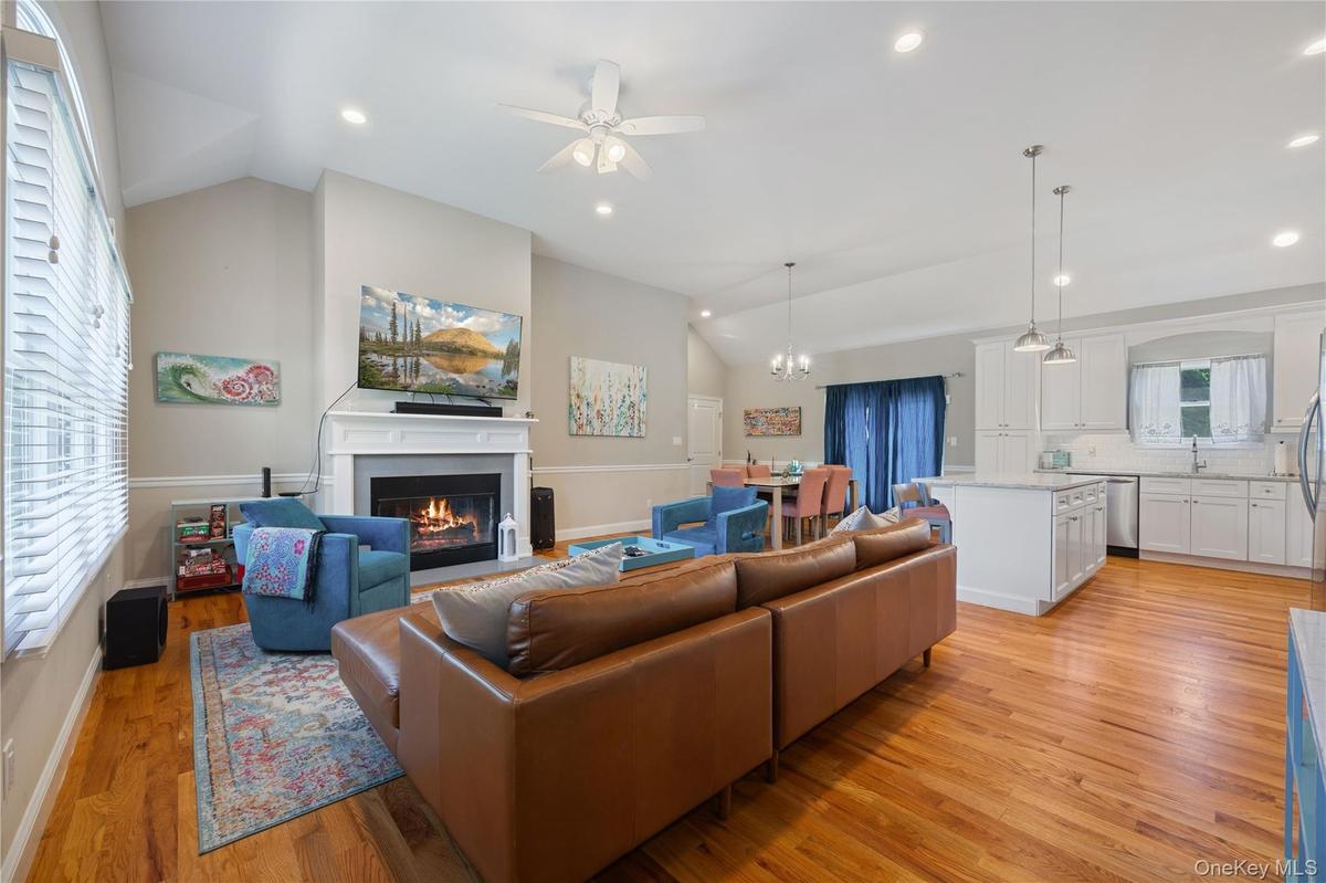 Living area featuring lofted ceiling, light wood-style floors, a fireplace with flush hearth, recessed lighting, and ceiling fan