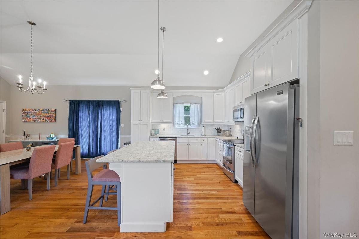 Kitchen featuring lofted ceiling, appliances with stainless steel finishes, white cabinetry, tasteful backsplash, and light wood-style flooring
