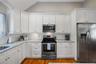 Kitchen featuring stainless steel appliances, white cabinetry, decorative backsplash, light stone counters, and light wood-type flooring