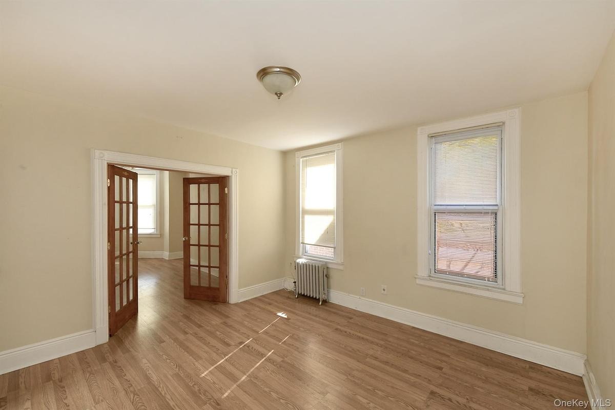 Empty room with french doors, wood finished floors, and radiator