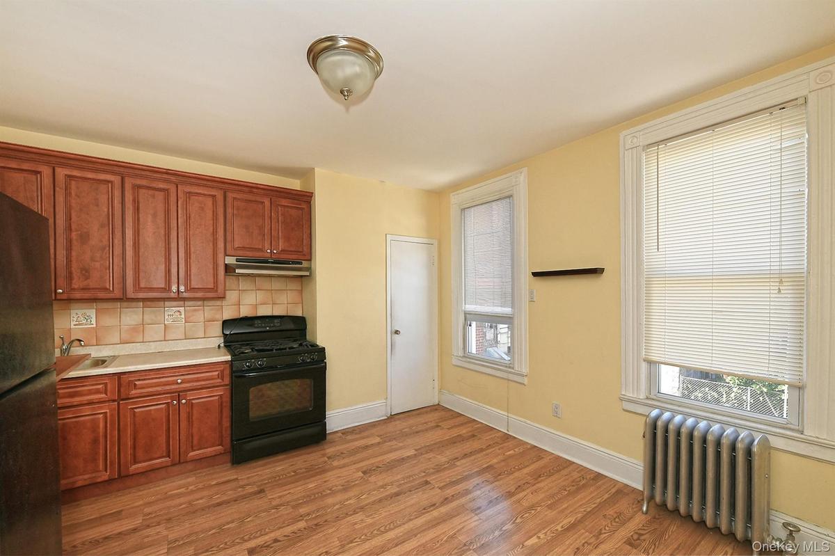 Kitchen featuring black appliances, radiator heating unit, tasteful backsplash, light countertops, and dark wood-style flooring