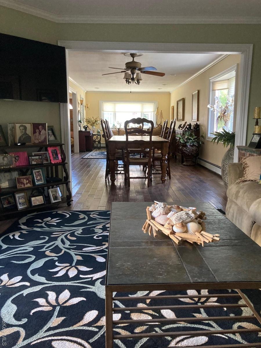 Living room with crown molding, dark wood-style floors, ceiling fan, and a baseboard radiator