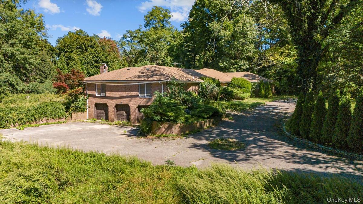 View of front of home featuring driveway, brick siding, a chimney, and view of side driveway