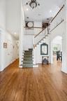 A secondary view of the magnificent entrance foyer, revealing its oak wood-finished floors, elegant arched walkways, and a sweeping stairway beneath t