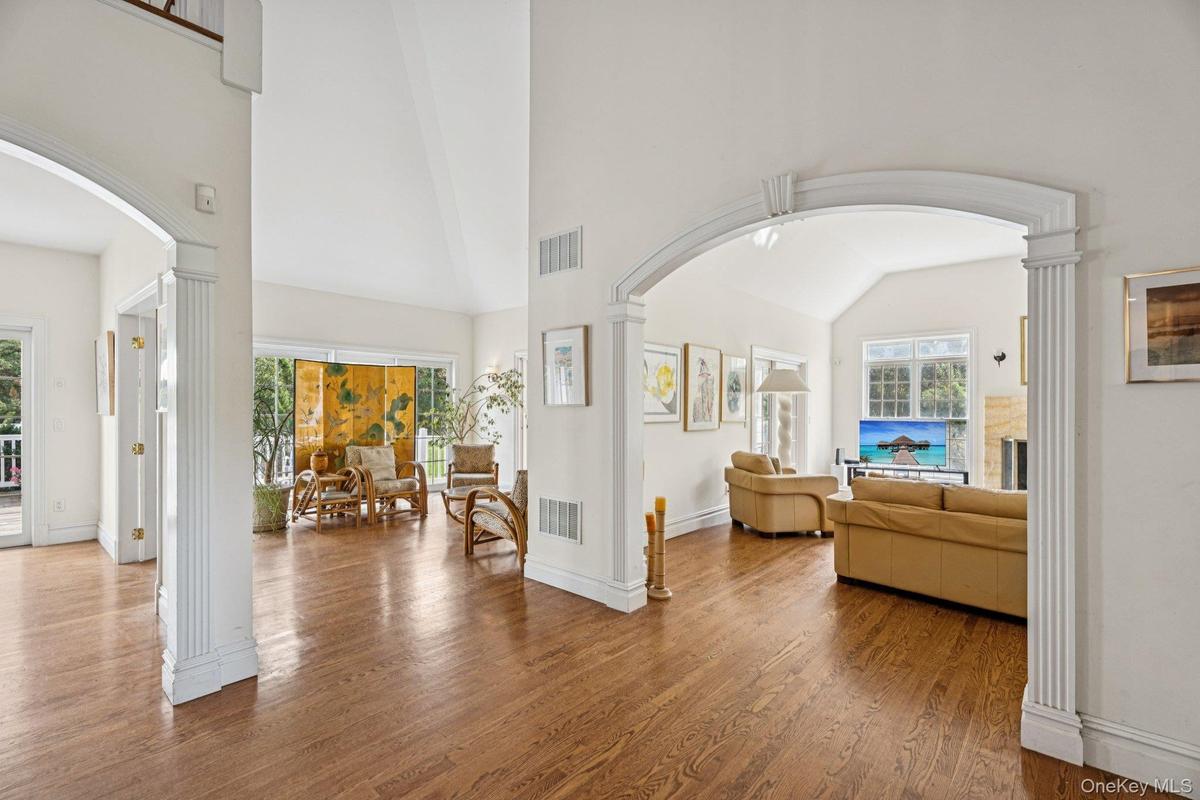 An impressive foyer adorned with oak flooring, vaulted cathedral ceilings, and arched walkways that lead to a sweeping grand stairway.