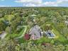 An aerial side perspective reveals the property’s architectural elegance, featuring a sunroom framed by floor-to-ceiling windows, and lushly landscape