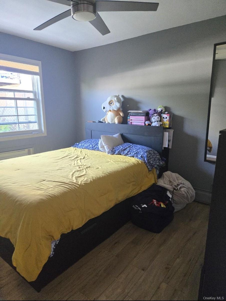 Bedroom featuring dark wood-style flooring, ceiling fan, and a baseboard heating unit