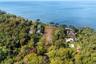 Aerial view highlighting the property’s prime position near the waterfront, surrounded by mature trees and neighboring residences, with the shoreline 