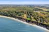 Sweeping aerial showcasing the property’s dramatic waterfront bluff setting, sandy shoreline below, and expansive North Fork landscape with water view