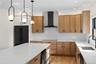 Kitchen featuring light stone counters, decorative light fixtures, wall chimney range hood, light wood-type flooring, and beverage cooler