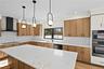 Kitchen with tasteful backsplash, light stone countertops, light wood-style flooring, wall chimney exhaust hood, and ornamental molding