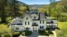 View of front of home with a chimney, a wooded view, a front yard, and a mountain view