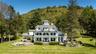 Shingle-style home featuring covered porch, a view of trees, a front yard, and a patio area