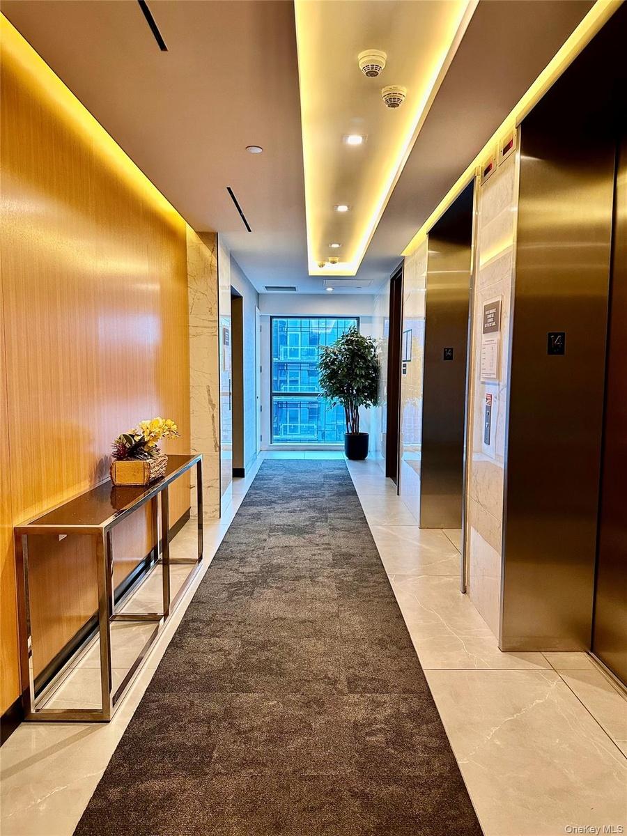 Hallway with elevator, light tile patterned flooring, recessed lighting, and expansive windows
