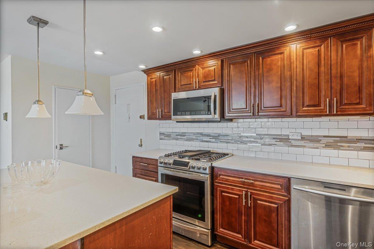 Kitchen featuring stainless steel appliances, hanging light fixtures, recessed lighting, tasteful backsplash, and light stone countertops