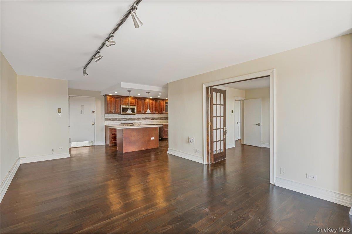 Unfurnished living room featuring rail lighting, dark wood finished floors, and french doors