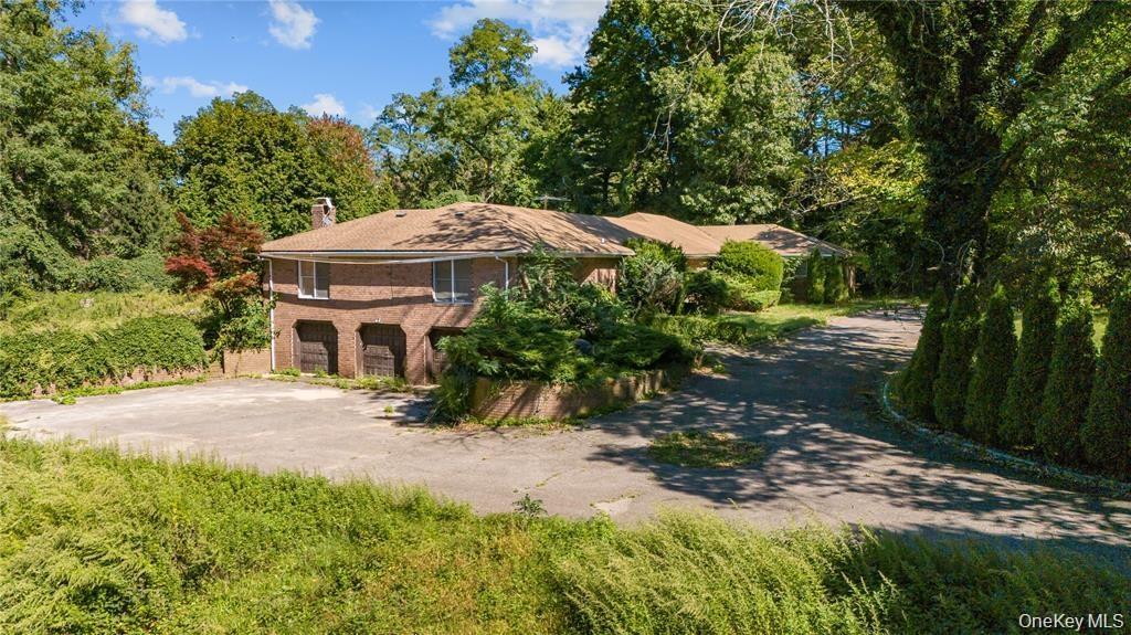View of front facade featuring a chimney, driveway, brick siding, and view of wooded area