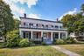 View of front of home with a chimney, brick siding, a front yard, and a porch