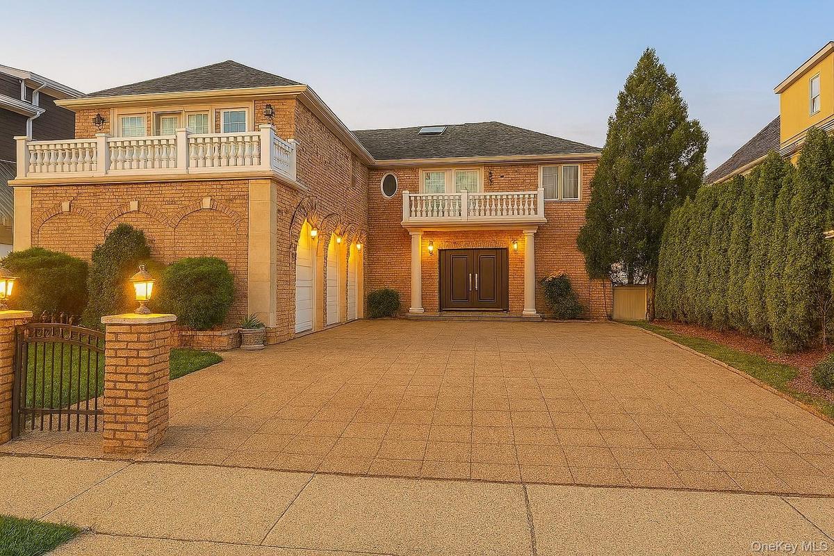 View of front of home with driveway, brick siding, a balcony, a gate, and a shingled roof