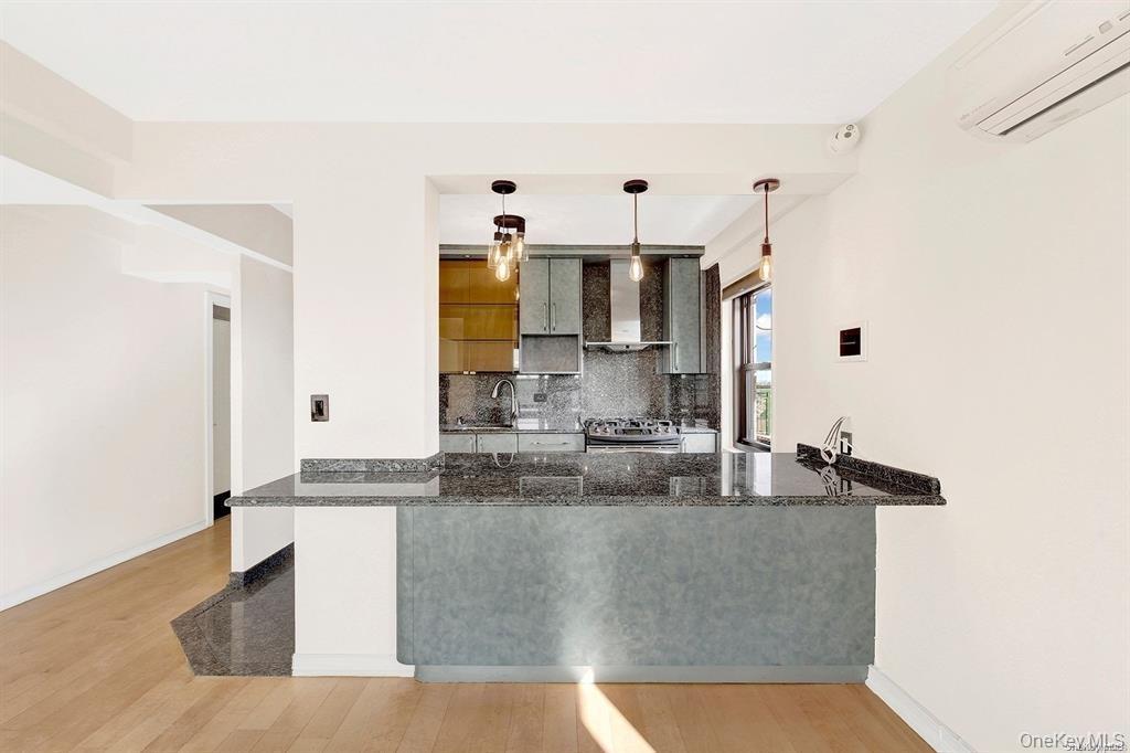 Kitchen featuring a peninsula, tasteful backsplash, a wall mounted AC, hanging light fixtures, and dark stone counters