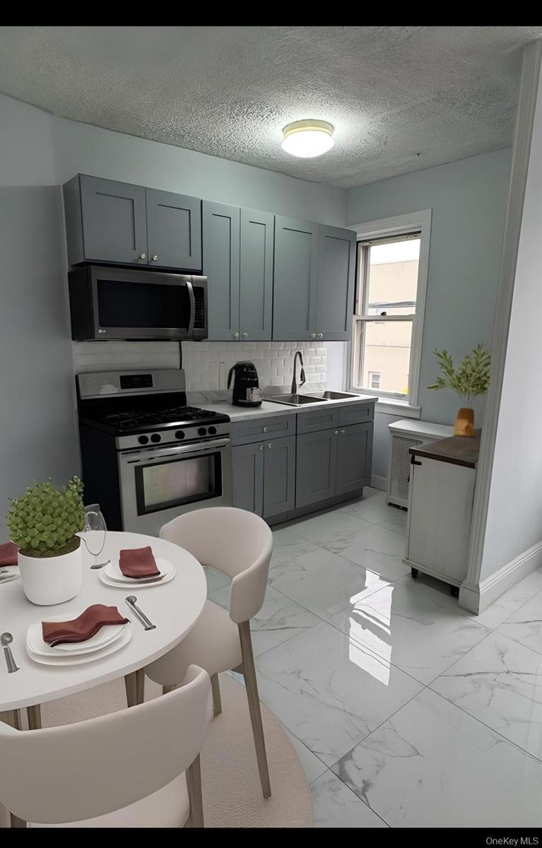 Kitchen featuring light marble finish flooring, gray cabinetry, stainless steel appliances, tasteful backsplash, and a textured ceiling